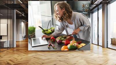 Happy young woman making a salad at the kitchen Wall mural