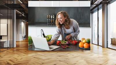 Happy young woman making a salad at the kitchen Wall mural