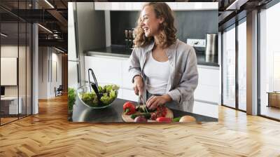 Happy young woman making a salad at the kitchen Wall mural