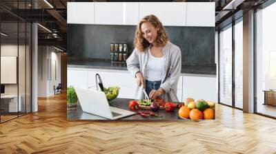 Happy young woman making a salad at the kitchen Wall mural