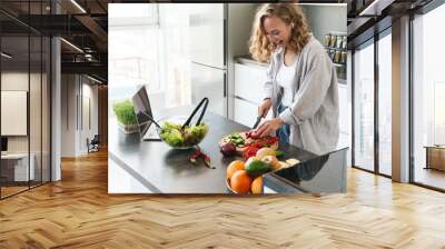 Happy young woman making a salad at the kitchen Wall mural