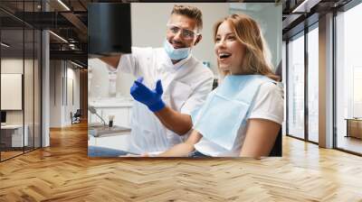 Happy young woman sitting in medical dentist center looking at x-ray scan. Wall mural