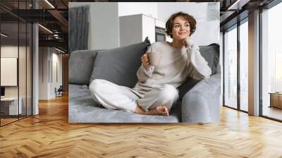 happy young woman sitting on a couch at home Wall mural