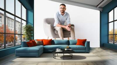 Horizontal portrait of attractive caucasian guy wearing stylish formal clothing sitting in armchair and looking at camera, isolated over white background Wall mural