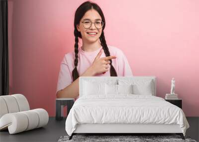 Image closeup of joyful happy girl with two braids wearing eyeglasses smiling and pointing fingers aside at copyspace Wall mural