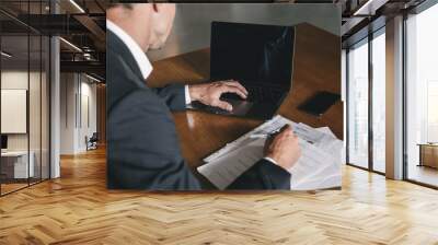 Image from back of businesslike man wearing white shirt and black suit sitting at table in office and looking at laptop, during work with documents Wall mural