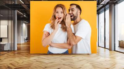 Image of attractive couple man and woman in basic t-shirts whispering secrets or gossips to each other Wall mural