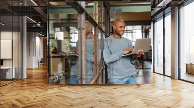 Image of bald african american man holding laptop while working in office Wall mural