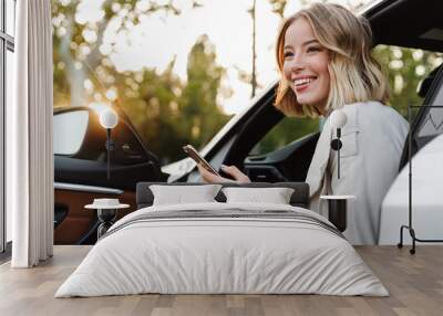 Image of beautiful businesslike woman sitting in car and using cellphone Wall mural