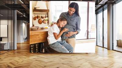 Image of beautiful family little girl listening to her pregnant mother's belly at cozy apartment Wall mural