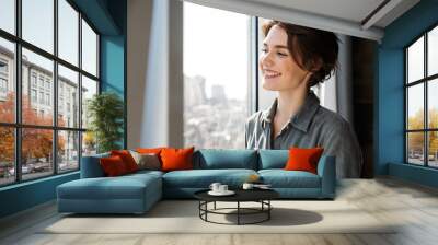 Image of beautiful young joyful woman smiling and looking at window Wall mural