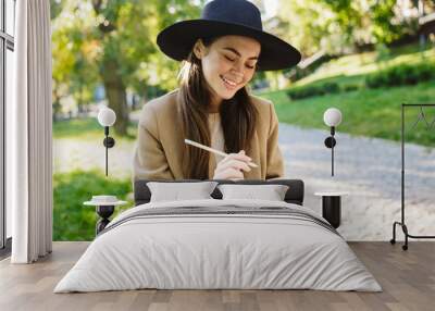 Image of brunette woman holding diary book while sitting on bench in park Wall mural