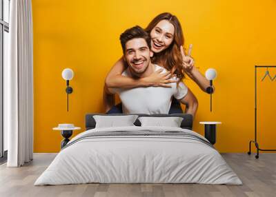 Image of caucasian couple having fun while man piggybacking joyful woman, isolated over yellow background Wall mural