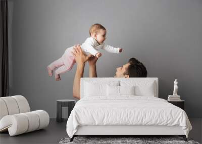 Image of caucasian father man holding his little baby in hands, isolated over gray background Wall mural