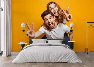 Image of caucasian man having fun and giving piggyback ride to joyful woman, isolated over yellow background Wall mural