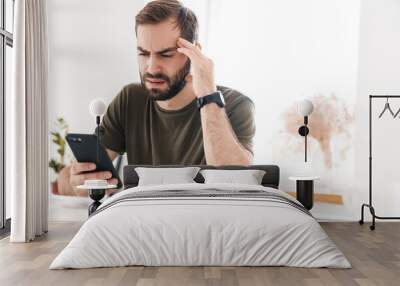 Image of caucasian tired man typing on cellphone while sitting Wall mural