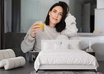 Image of caucasian woman 30s drinking orange juice, while resting in bright modern house Wall mural