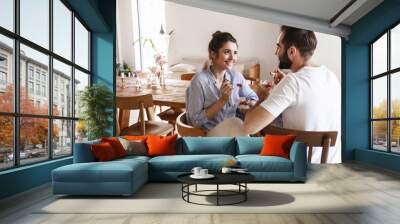 Image of cheerful brunette couple eating panna cotta dessert together while sitting at table at home Wall mural