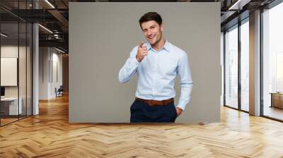 Image of cheerful brunette man wearing formal clothes smiling and pointing finger at camera while winking Wall mural