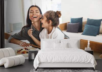 Image of cheerful family mother and little daughter smiling and eating together while having breakfast at home in morning Wall mural