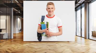 Image of european student boy wearing backpack smiling and posing at camera with colorful exercise books in hands, isolated over white background Wall mural