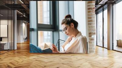 Image of focused woman reading book while sitting in armchair Wall mural