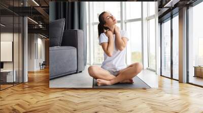 Image of focused young woman stretching her neck while sitting on yoga Wall mural