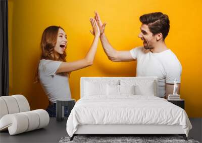 Image of friendly young people man and woman in basic clothing laughing and giving high five, isolated over yellow background Wall mural