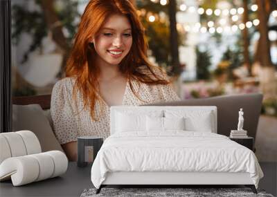 Image of ginger girl smiling and working with laptop while sitting Wall mural