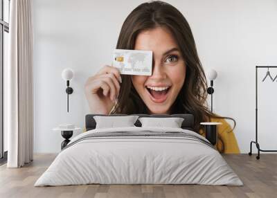 Image of gorgeous brunette woman wearing casual clothes smiling and holding credit card Wall mural