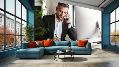 image of handsome businessman talking on cell phone while working on computer in office Wall mural