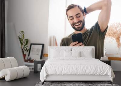 Image of handsome laughing man typing on laptop and using cellphone Wall mural