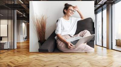 Image of happy beautiful woman using laptop while sitting on sofa Wall mural