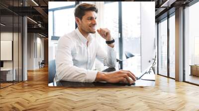 Image of happy businesslike man sitting at table and working on computer in office Wall mural