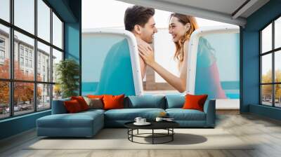 Image of happy couple laughing and looking at each other while sitting Wall mural