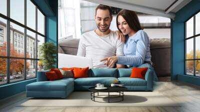 Image of happy couple using laptop together while sitting on sofa in living room at home Wall mural