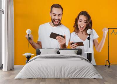 Image of happy man and woman playing together video games on smartphones, isolated over yellow background Wall mural