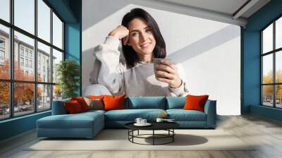 Image of happy woman 30s holding cup with tea, while sitting over white wall indoor Wall mural