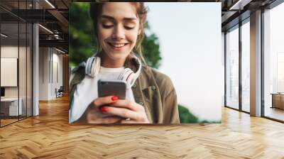 Image of happy woman holding smartphone and walking in green park Wall mural