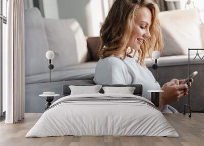 Image of happy woman smiling and using cellphone while sitting on floor Wall mural