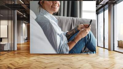 Image of happy woman smiling and using cellphone while sitting on sofa Wall mural