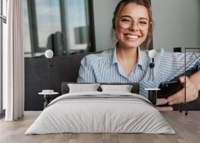 Image of happy young woman in eyeglasses smiling and using cellphone Wall mural