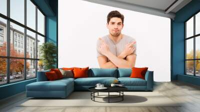 Image of indecisive man wearing beige t-shirt gesturing fingers aside with crossed arms on two copyspace options, isolated over white background Wall mural