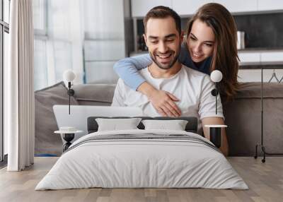 Image of joyful couple using laptop together while sitting on sofa in living room at home Wall mural