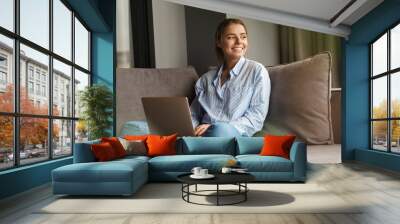 Image of joyful woman using laptop and smiling while sitting on sofa Wall mural