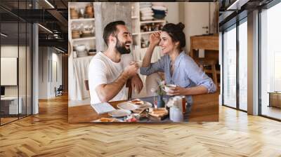 Image of modern brunette couple eating breakfast together while sitting at table at home Wall mural