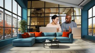 Image of multiethnic young coworkers working on laptops in office Wall mural