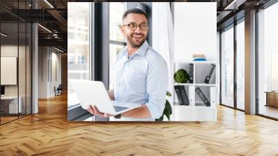 image of office worker man wearing white shirt looking aside, while holding silver laptop during wor Wall mural