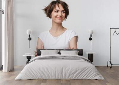 Image of optimistic woman in basic t-shirt smiling and looking aside while standing with arms crossed Wall mural