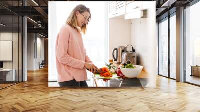 Image of pleased cute woman in eyeglasses smiling and making lunch Wall mural